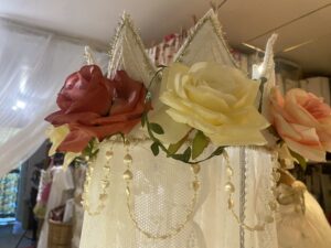 Un ciel de lit avec des rideaux en dentelles et une couronne en feutrine et des roses artificielles. 